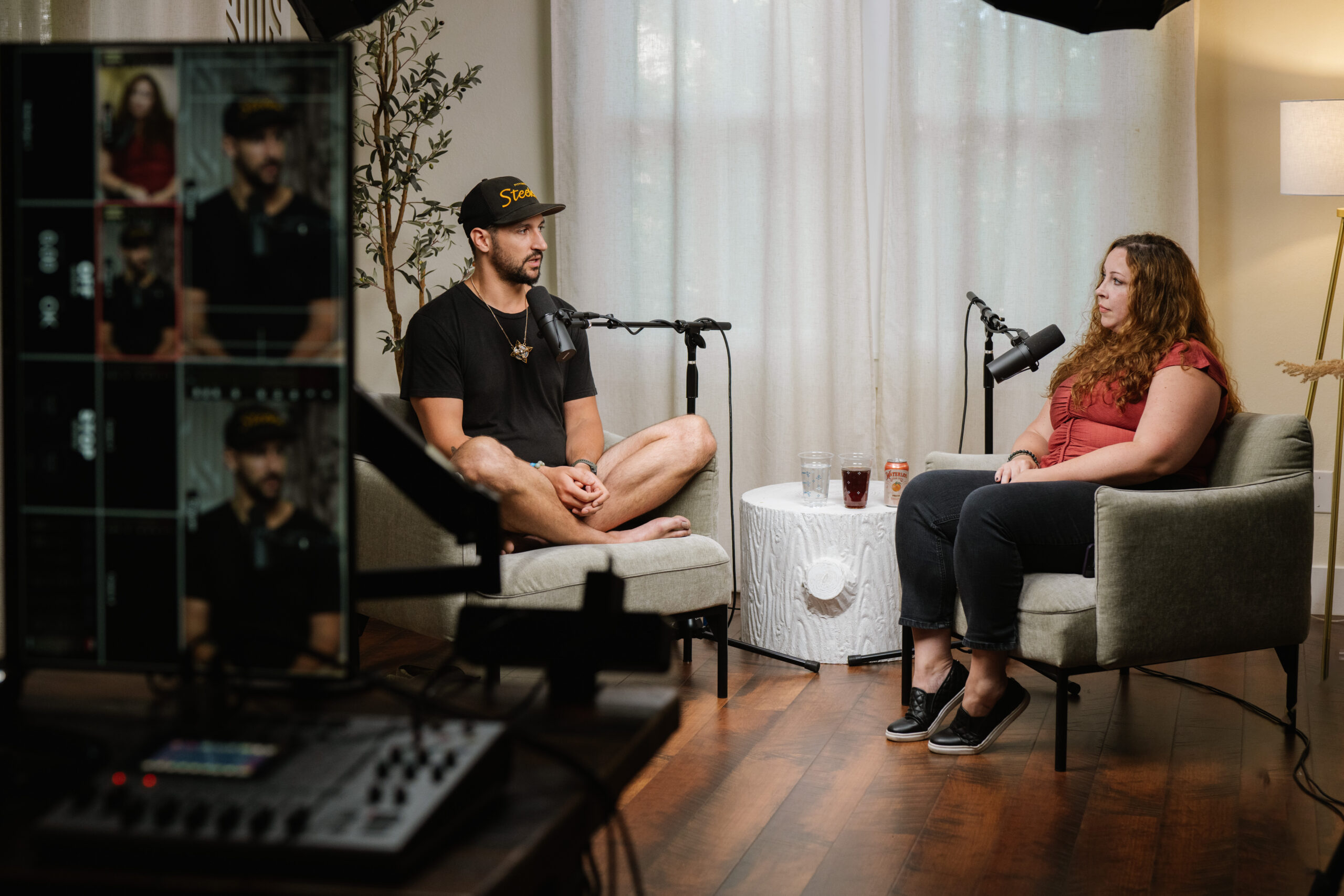 two podcasters sit on armchairs in a professional studio facing each other